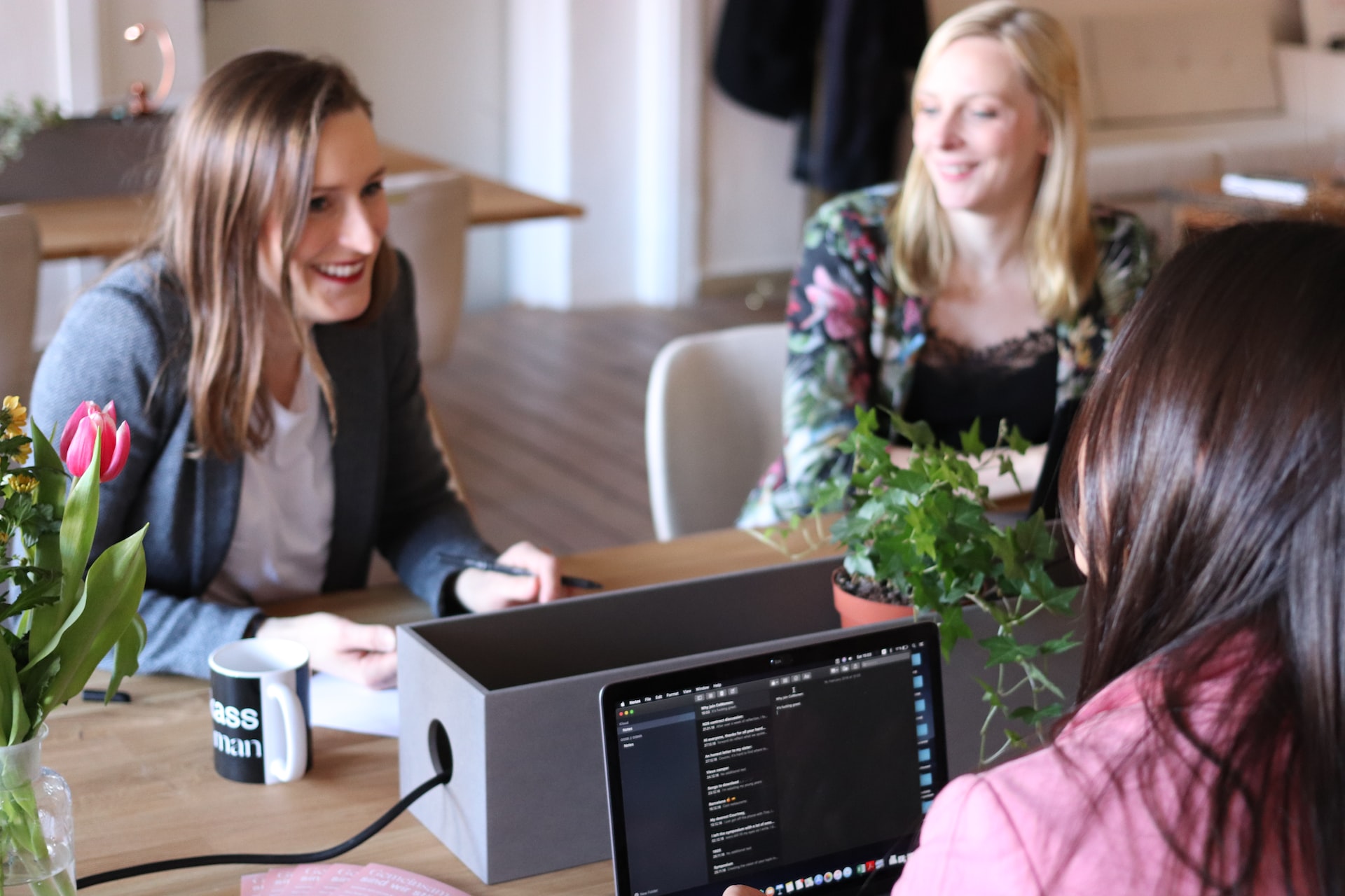 Group of female technology workers smiling while collaborating seated at a table.
